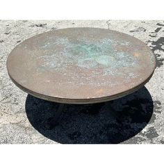 a round metal table sitting on top of a cement ground next to a black and white floor