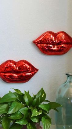 two red lips are hanging on the wall next to a potted plant and vase