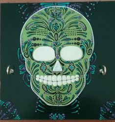 a green and blue skull with ornate designs on it's face is shown in front of a black background