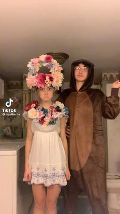 two people in costumes standing next to each other with flowers on their heads and one person wearing a bear costume