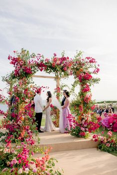 a couple getting married in front of an arch with pink and red flowers on it