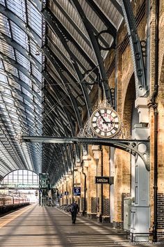 a train station with a clock hanging from the ceiling and people walking on the platform