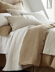 a bed with white and brown linens in a bedroom next to a window on a wooden floor