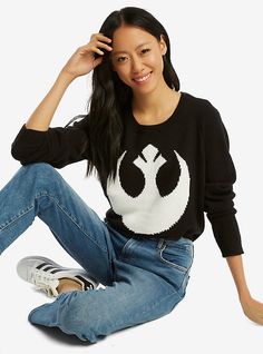 a woman sitting on the floor wearing a star wars sweater and jeans with her legs crossed