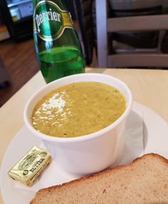 a white plate topped with a bowl of soup next to a slice of bread and a bottle of beer