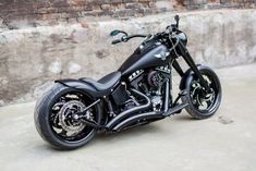 a black motorcycle parked on top of a cement floor next to a brick wall in front of a building