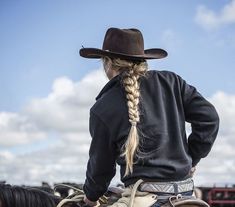 a woman wearing a cowboy hat and braids on top of a horse's back