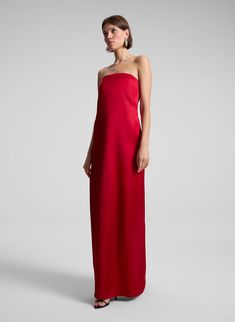 The Ani Gown is crafted from rich structured satin in a striking red hue. This '90s-inspired silhouette features a straight strapless neckline, concealed bone corsetry and a sleek column shape, embodying minimalist elegance with clean lines. This style runs small, we recommend taking one size up from your usual size. Shop Dresses. Styling Tip: Pair with tonal heels and a sleek clutch for a refined and modern evening look. Strapless Sheath Dress, 2025 Fashion, Strapless Neckline, Red Gowns, Handmade Dress, Satin Gown, Women's Wear, 90s Inspired, Handmade Dresses