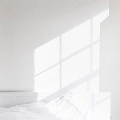 a bed with white sheets and pillows in a room next to a window that has blinds on it