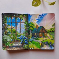 an open book with a painting of a house in the window and flowers around it