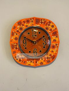 an orange and black clock on the wall with numbers painted on it's face