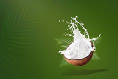 a coconut with milk splashing out of it on a green and leafy background