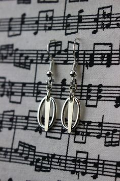 two pairs of silver earrings with musical notes in the background on a sheet of music paper