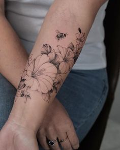 a woman's arm with flowers on it and a bee flying over the top