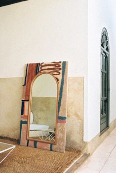 a large mirror sitting on top of a floor next to a wall with a chair