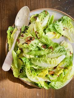 a bowl filled with lettuce on top of a wooden table next to a spoon