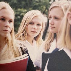 three young women standing next to each other with books in their hands and looking at the camera