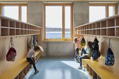 three children are sitting on benches in a room with bookshelves and large windows