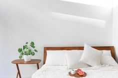 a bed with white sheets and pillows in a bedroom next to a small wooden table