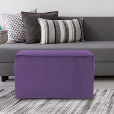 a purple ottoman sitting on top of a rug next to a gray couch and pillows