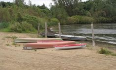 three canoes are sitting on the sand near some water and trees in the background