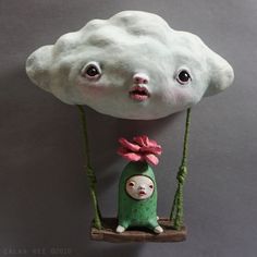 there is a cloud with a face on it and a doll hanging from the side