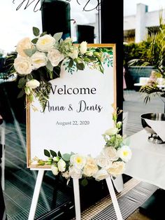 a welcome sign sitting on top of a wooden easel next to a window filled with flowers