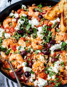 a skillet with shrimp, olives, feta cheese and bread on the side