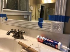 a bathroom sink with blue tape on the edge and a mirror above it, next to a tube of toothpaste