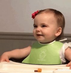 a baby in a green bib smiling at the camera