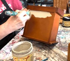 a person is painting the inside of a wooden frame on a table with paintbrushes