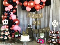 a table topped with lots of cakes and desserts next to a skeleton balloon arch