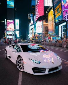 a white sports car parked on the side of a street in times square at night