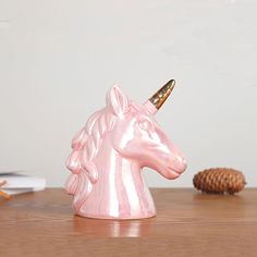 a pink ceramic unicorn figurine sitting on top of a wooden table next to a pine cone