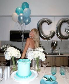 a woman sitting at a table in front of a cake with balloons and flowers on it