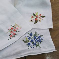 three embroidered napkins with flowers on them sitting on a wooden table next to each other