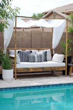 a couch sitting next to a swimming pool under a pergolated trellis with white drapes