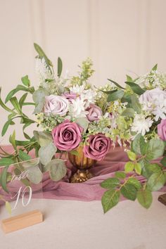 a vase filled with pink and white flowers on top of a table next to a wooden sign