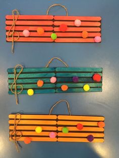 three popsicle craft sticks with pom - poms tied to them on a table