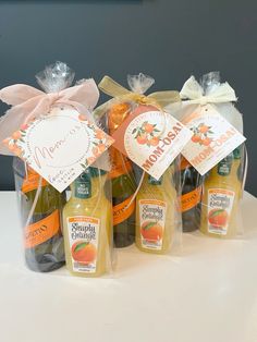 four bottles of orange juice in cello bags on a white table with a pink bow