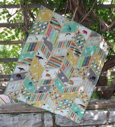 a quilt is sitting on a wooden bench in front of a tree and stone wall