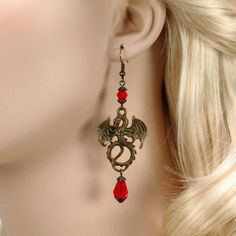 Lady Pendragon Antique Bronze and Ruby Red Dragon Earrings with Teardrop Crystal As fearsome as they are mysterious, dragons have long been the subject of Medieval lore. Create a unique and memorable Medieval or Renaissance-inspired cosplay with the inspiration of the bold Lady Pendragon red dragon earrings.These mythical earrings feature an antique bronze winged dragon crowned by a light-catching ruby red crystal. Dangling below, a matching teardrop crystal adds a touch of color and movement. W Winged Dragon, Teardrop Pearl Earrings, Dragons Crown, Dragon Earrings, Blue Dangle Earrings, Dragon Wings, Red Dragon, Red Crystals, Silver Filigree