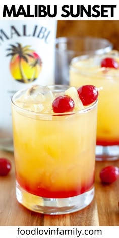 two glasses filled with drinks and cherries on top of a wooden table next to a bottle