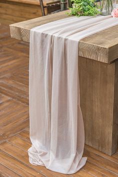 a wooden bench with a white table cloth draped over it and flowers on the back