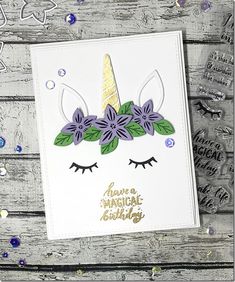 a card with an unicorn's face and purple flowers on it, surrounded by confetti