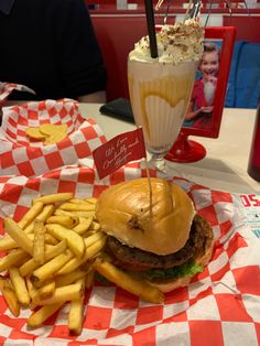 a hamburger and fries on a red and white checkered paper with a drink in the background