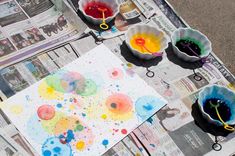 several bowls filled with paint sitting on top of a newspaper next to other paints and paper