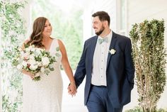 a bride and groom holding hands walking down the aisle with greenery on either side