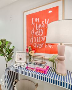 a desk with a lamp, vase and pictures on it in front of a painting