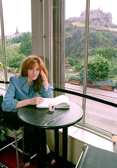 a woman sitting at a table with a book in front of her and looking out the window